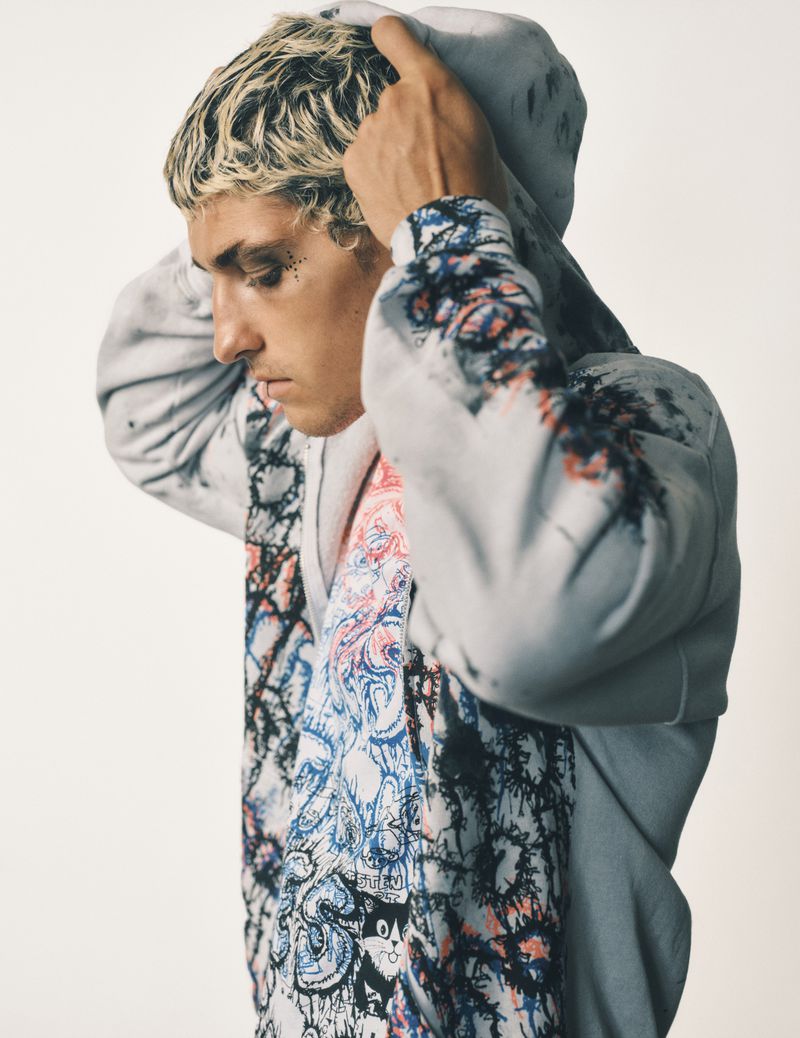 Young adult male in a grey patterned hoodie putting up the hood, casual fashion in a neutral background in a studio shot.