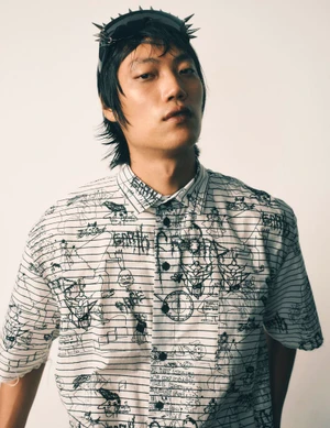 Asian man wearing a graphic printed button-down shirt and spiked headband against a white background