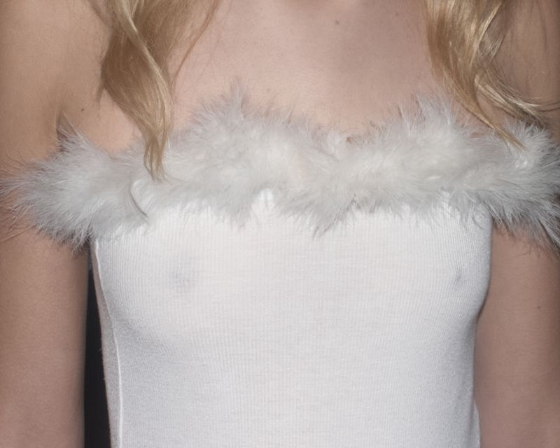 Close-up of a fair-skinned person wearing a white top with feather trim, creating a soft and textured effect against a dark backdrop.