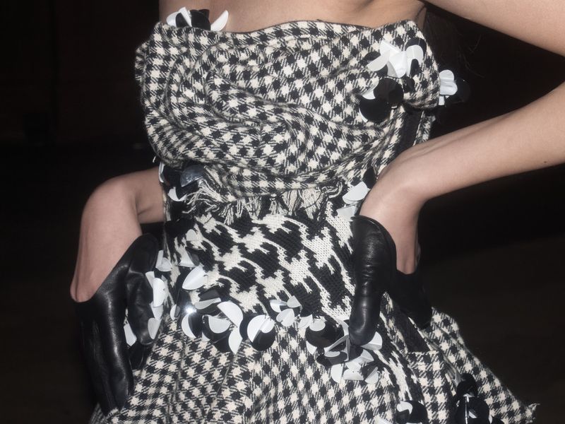 Woman in strapless dress with black and white houndstooth pattern, adorned with black and white floral embellishments and long gloves.