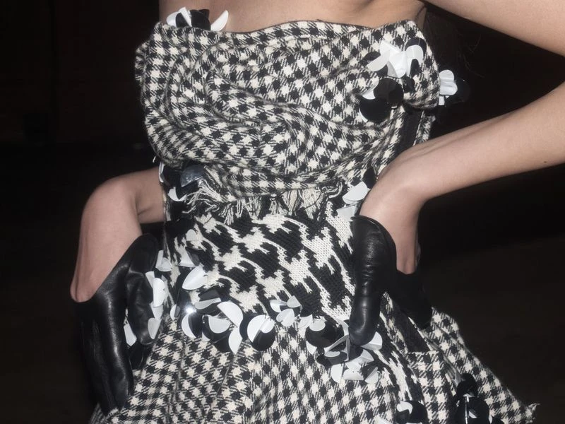 Woman in strapless dress with black and white houndstooth pattern, adorned with black and white floral embellishments and long gloves.