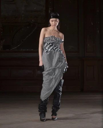 Model wearing a black and white houndstooth strapless dress and tall leather boots standing indoors