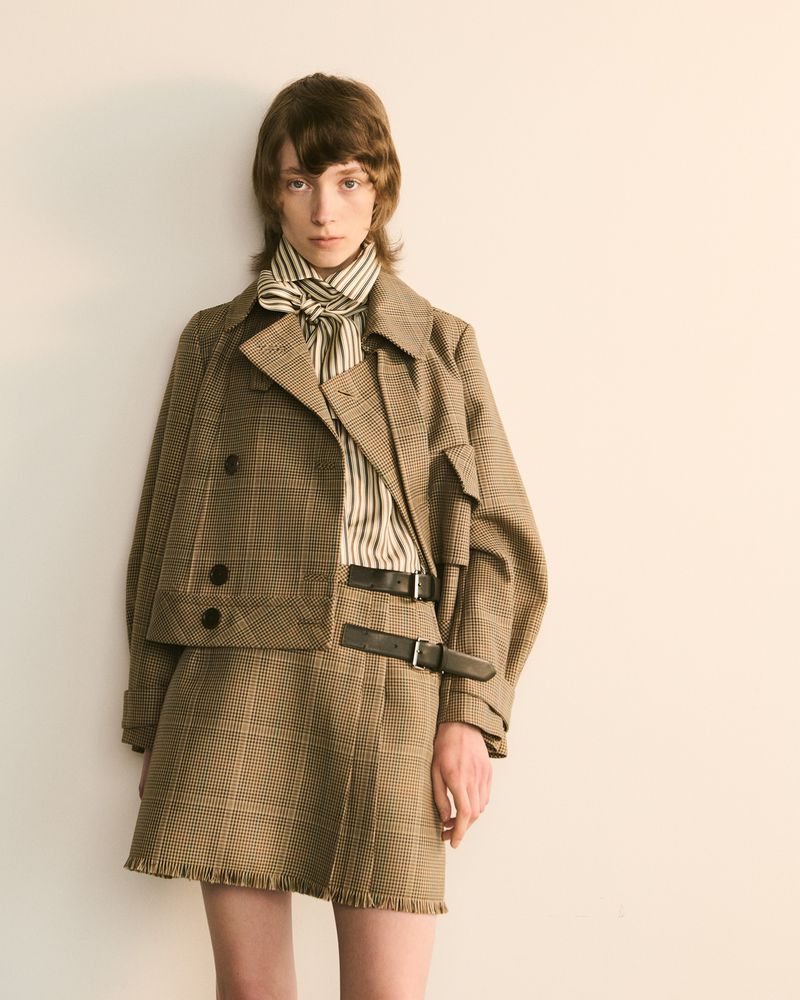 Fashion model in a houndstooth jacket and skirt with a striped top, posing in a studio with neutral lighting.  Fashion editorial shoot.