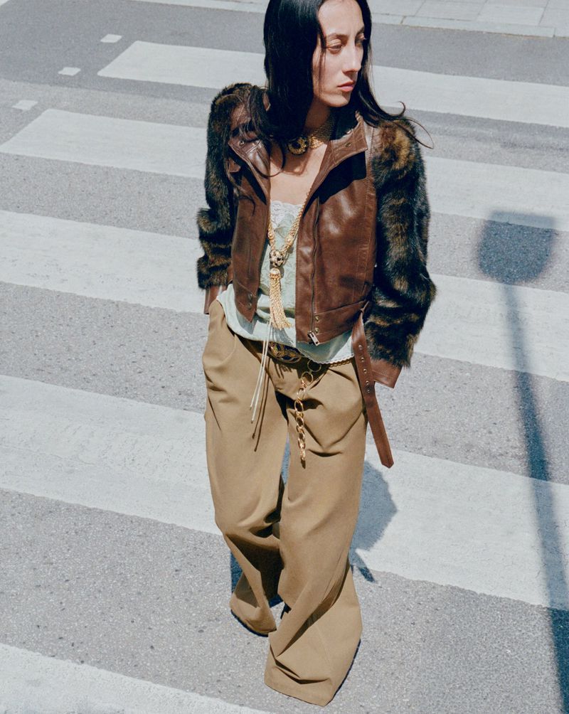 Model in brown leather jacket and wide trousers walking across a zebra crossing for Net-A-Porter