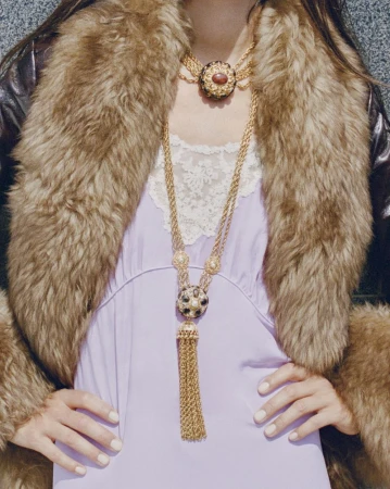 Model wearing a lavender dress, gold chain necklaces, and a brown fur collar jacket for Net-A-Porter
