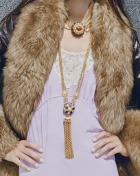 Model wearing a lavender dress, gold chain necklaces, and a brown fur collar jacket for Net-A-Porter