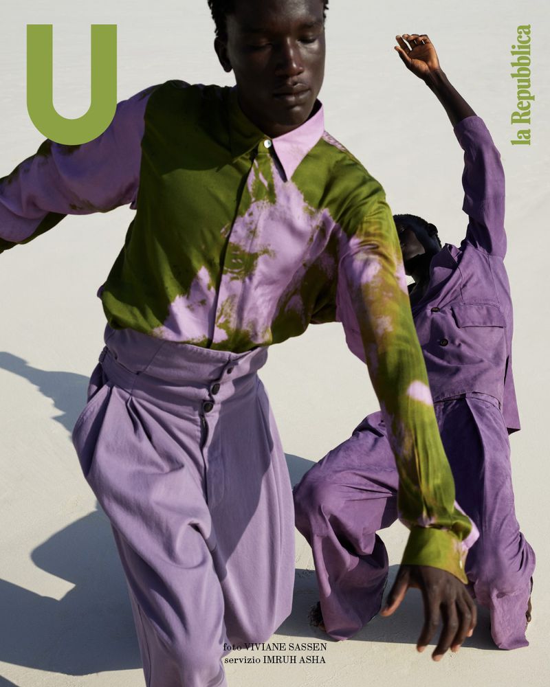 Editorial fashion shot of two Black male fashion models wearing colorful shirts and lavender pants against a neutral backdrop.