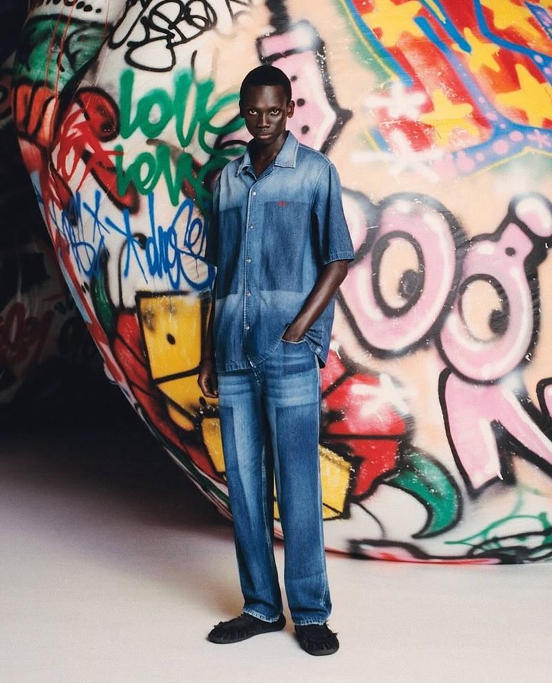 Man in matching denim shirt and pants standing in front of a graffiti-covered surface, casual fashion style, studio shot.
