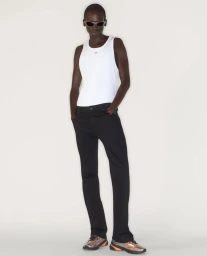 Model wearing a white tank top and dark pants against a plain white background