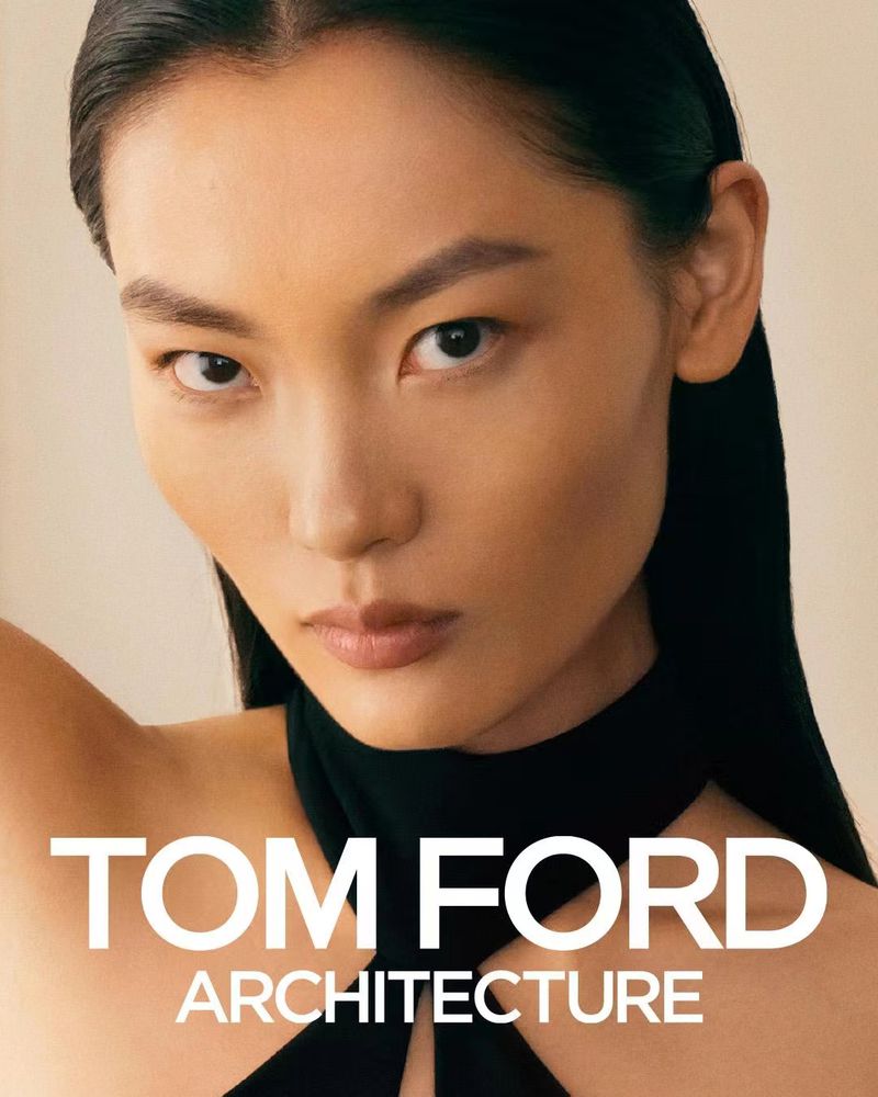 Close-up portrait of model Shan Li with slicked-back dark hair wearing a black top against a pale neutral background