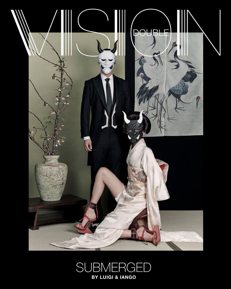 Editorial fashion shot featuring a man in a suit and a woman in a kimono, both wearing horned masks, set against a neutral backdrop.