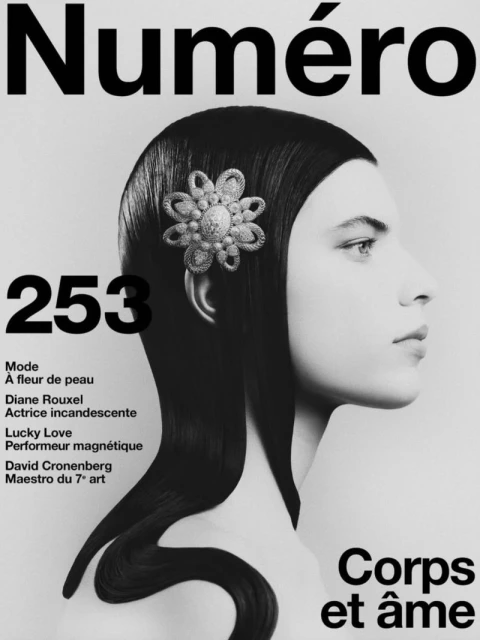 Black and white magazine cover featuring a woman in profile with sleek black hair, adorned with a jeweled flower embellishment.