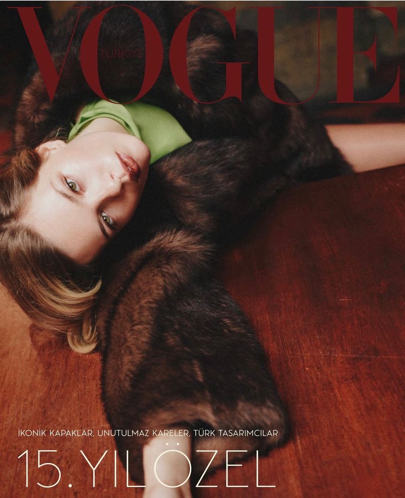 Vogue cover featuring a blonde woman in a fur coat and green top lying on a brown surface, magazine text in the background.