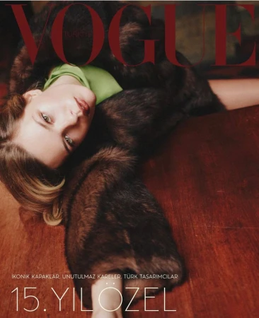 Vogue cover featuring a blonde woman in a fur coat and green top lying on a brown surface, magazine text in the background.
