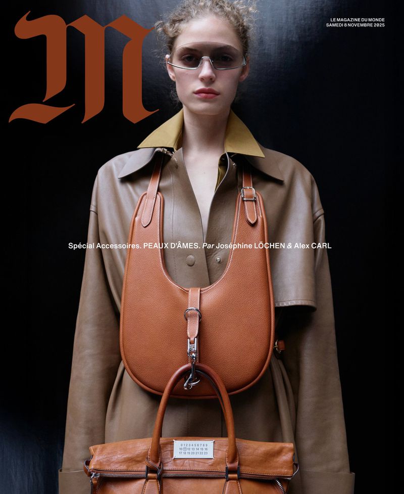 Magazine cover featuring a model in a tan trench coat with two brown leather bags against a dark backdrop, showcasing fashion and accessories.