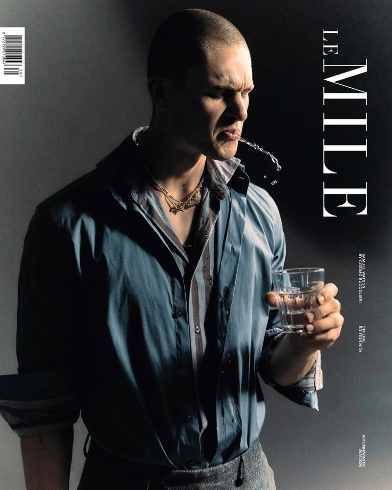 Magazine cover featuring a man in a blue shirt spitting out water from a glass, against a gradient black and grey background.