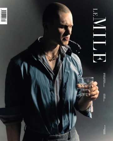 Magazine cover featuring a man in a blue shirt spitting out water from a glass, against a gradient black and grey background.