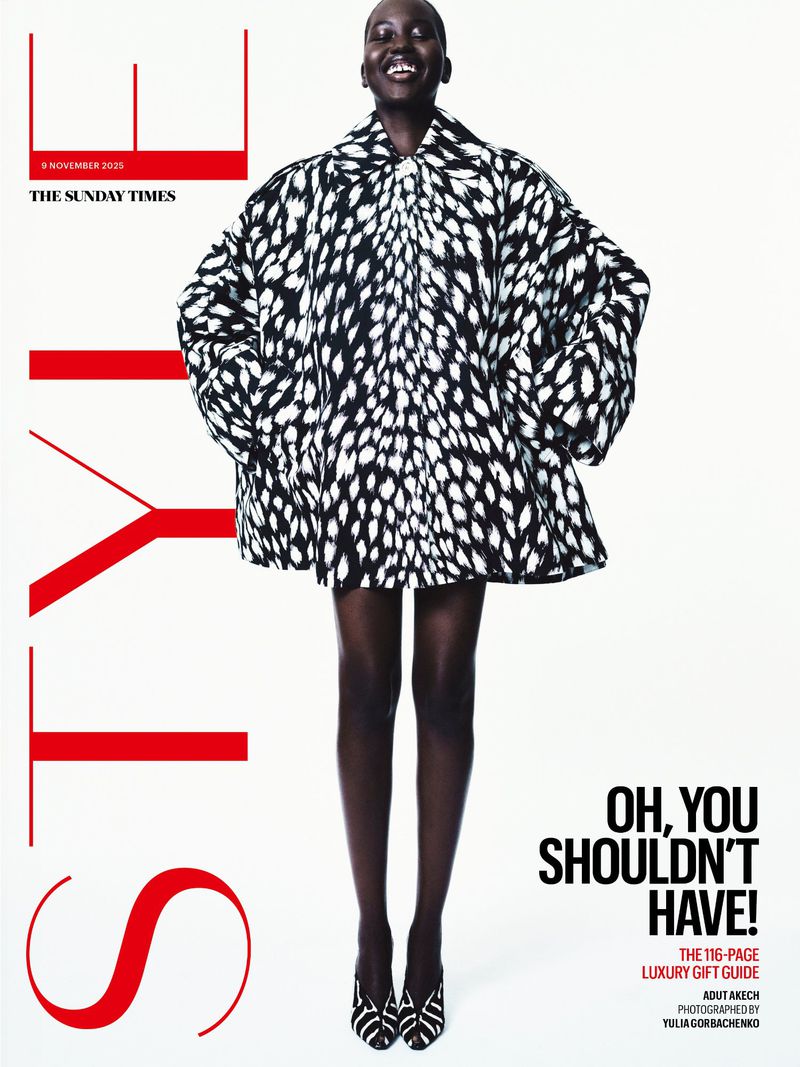 An African-American woman poses for a magazine cover, wearing a large black-and-white coat, black stockings and heels against a white background.