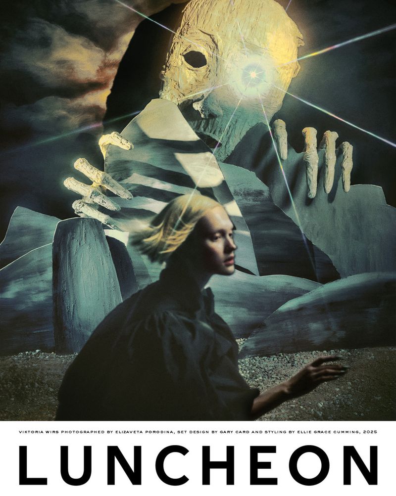 Fashion editorial featuring a blonde model in dark clothing posing in front of an eerie landscape with a surreal giant face.