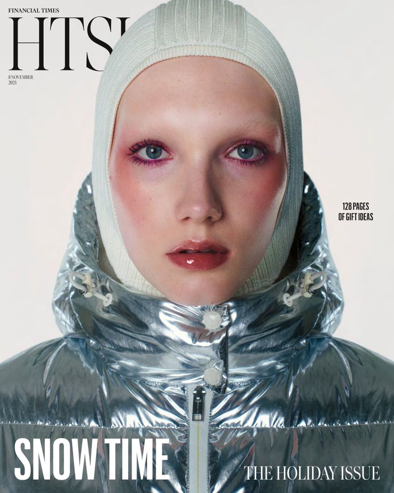 Close-up fashion magazine cover featuring a model in a silver puffer jacket and cream balaclava, with glossy lips and blush makeup.