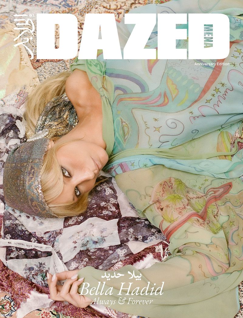 Bella Hadid lies on a vintage floral quilt, wearing a sparkling head covering and a printed sheer dress for a fashion magazine cover.