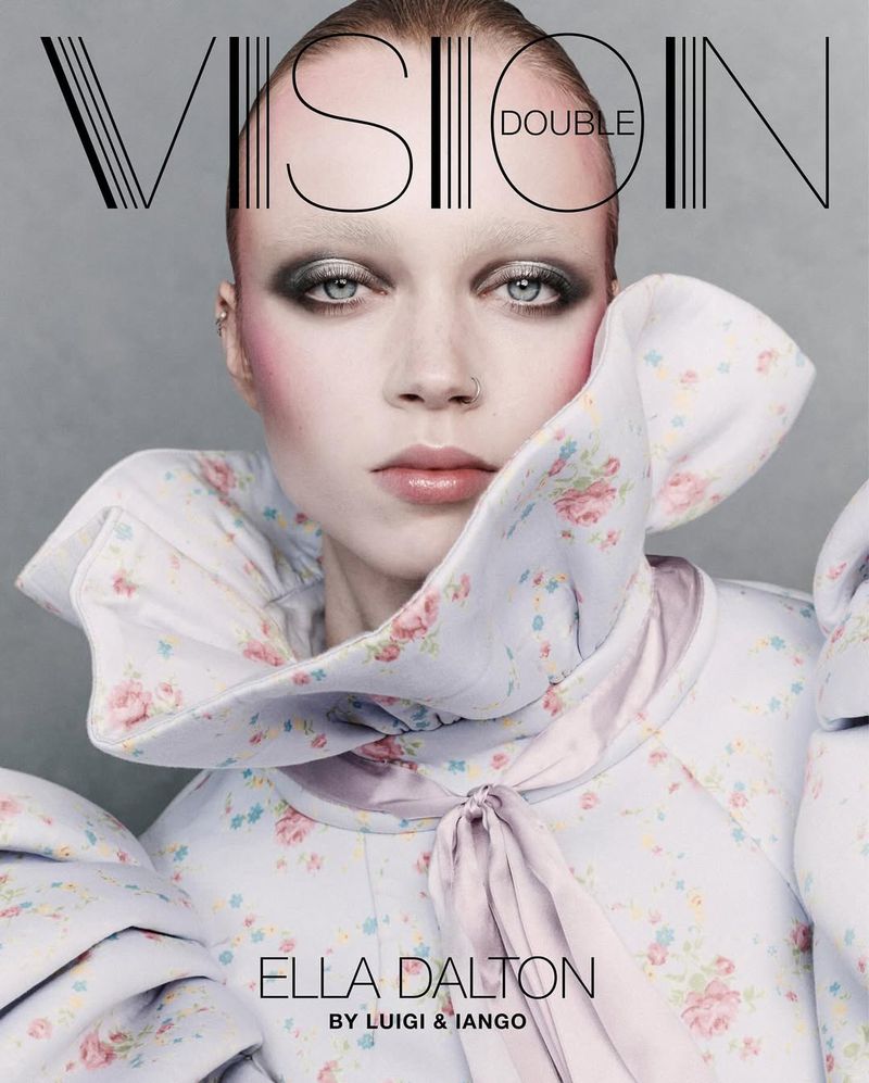 Close-up of a woman with striking makeup, wearing a floral-patterned garment, posing for a magazine cover with prominent text.