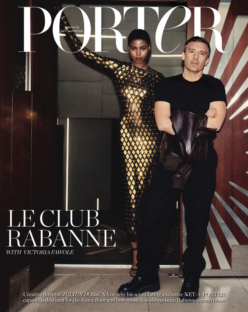Magazine cover featuring a fashion model in a gold dress standing beside a man in black attire, indoors, against a striped wall.