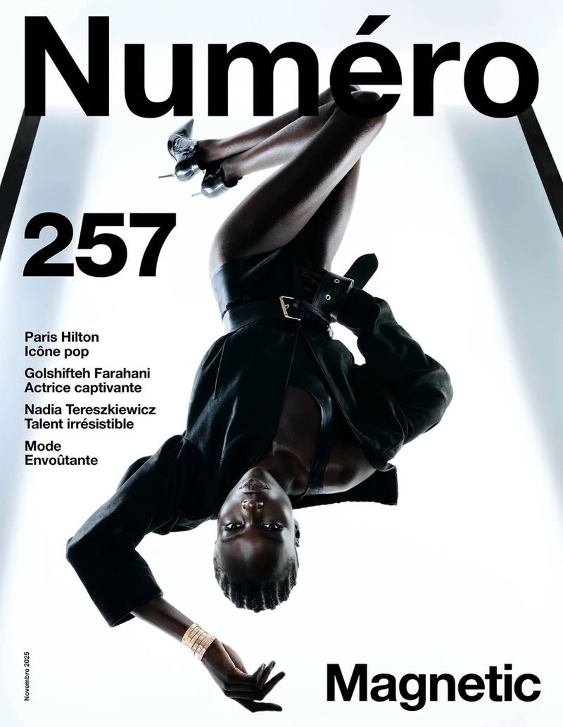 Magazine cover featuring a woman with dark skin and black hair, wearing black clothing, suspended upside down against a white backdrop.
