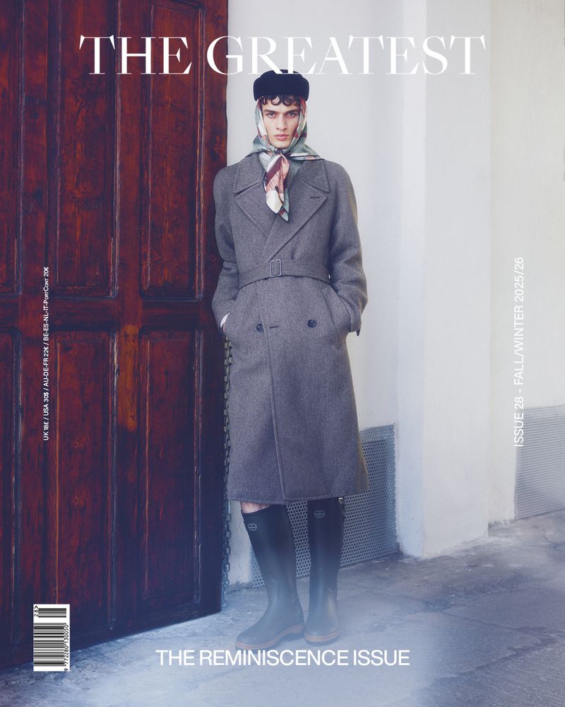 Magazine cover featuring a man in a gray overcoat, black cap, and rain boots, standing against a light wall next to a dark wooden door.