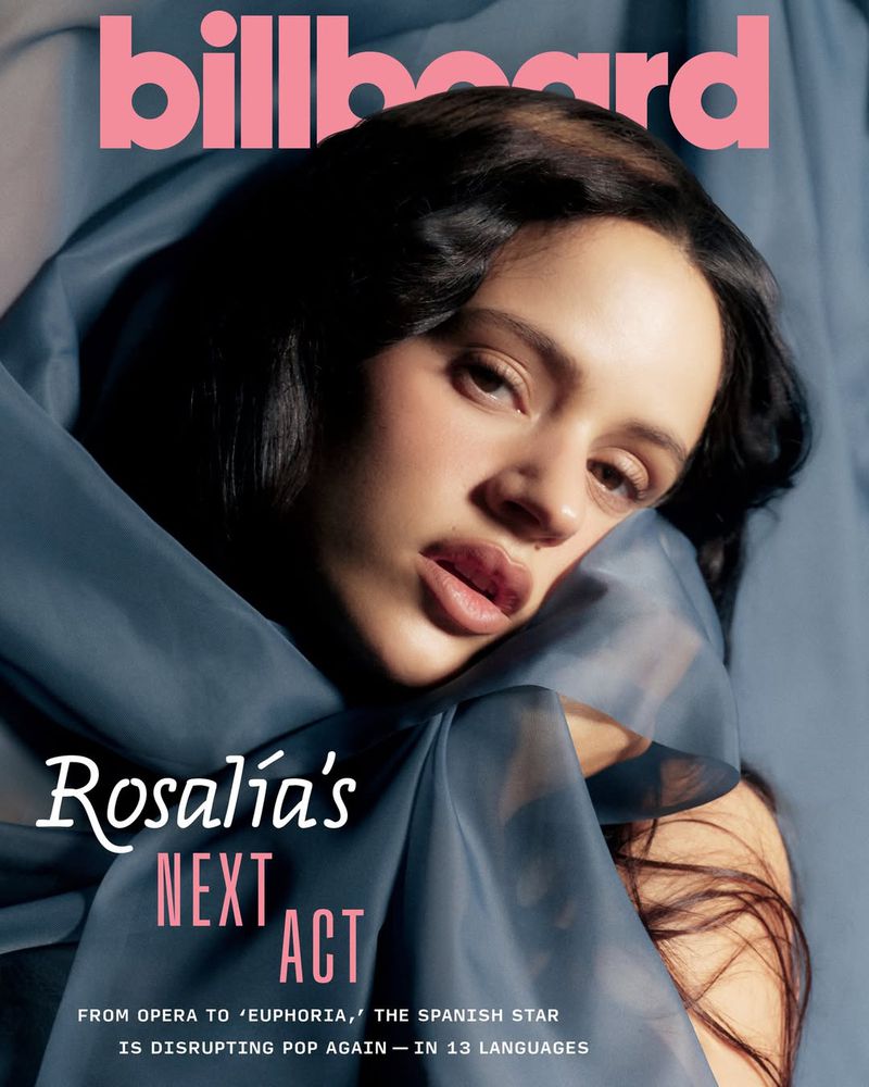 Billboard cover featuring Rosalía with dark hair and sheer blue fabric draped over her shoulders. Close-up, face and shoulders visible.