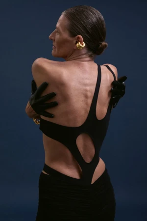 Model Guiomar Alfaro in black cutout dress with black gloves and gold ear cuff against dark background