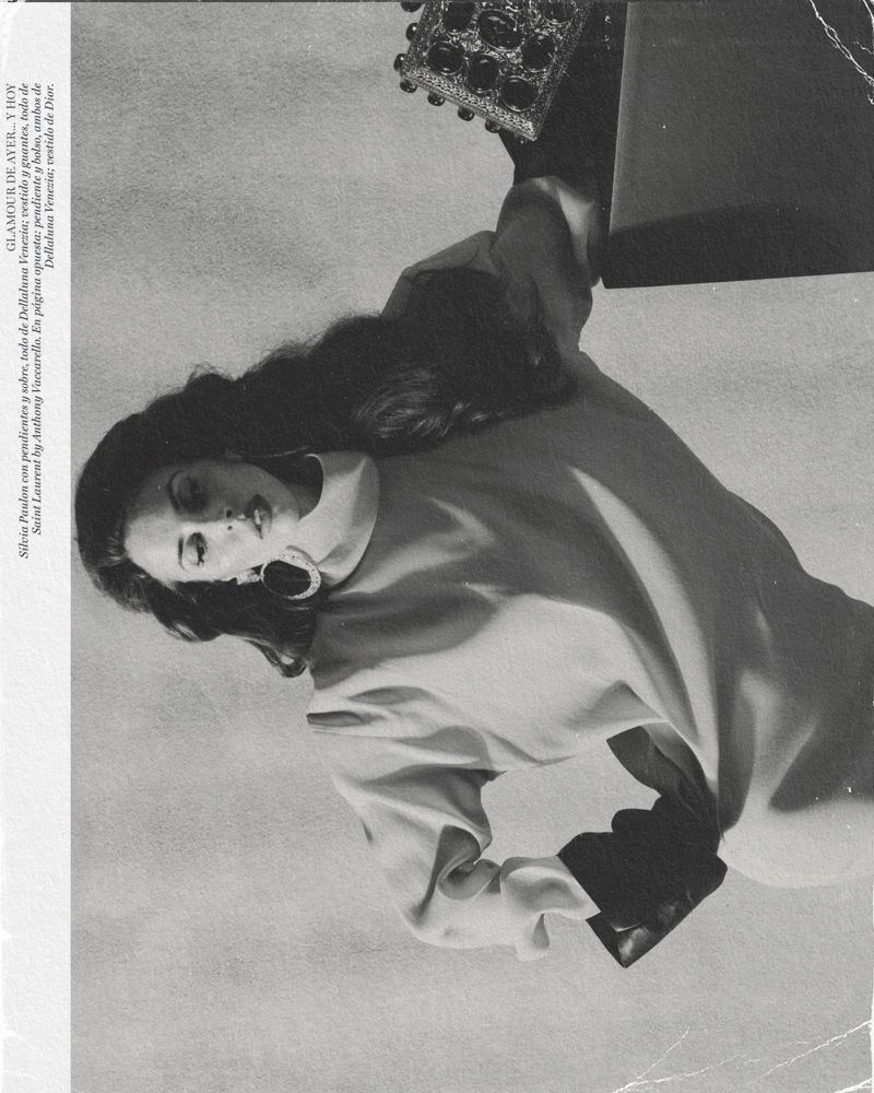 Black and white photograph of a woman wearing a light-colored dress, posing near a purse and another covered object.