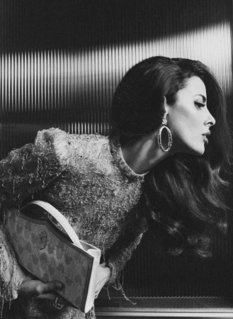 Black and white portrait of a woman with long dark wavy hair wearing large hoop earrings and holding a handbag