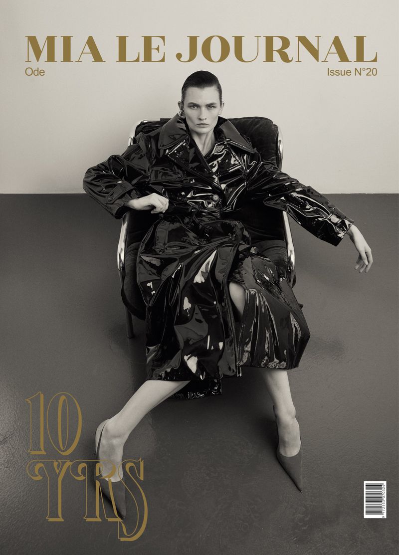 Magazine cover featuring a model in a glossy black trench coat sitting in a chair against a neutral backdrop, with bold typography.