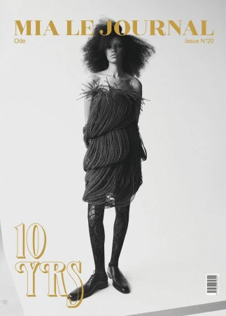 Magazine cover featuring a Black model in a unique braided dress, black patterned tights, and dress shoes against a white backdrop.