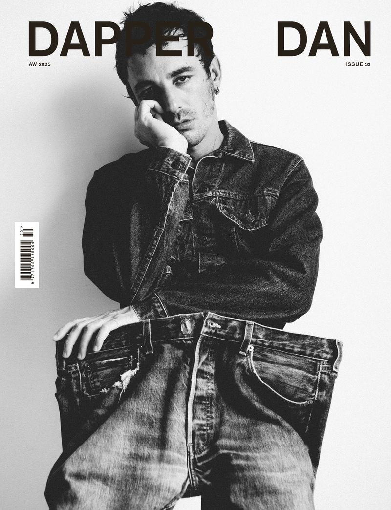 Black and white magazine cover featuring a seated man wearing a denim jacket and holding out the waistband of oversized denim jeans.