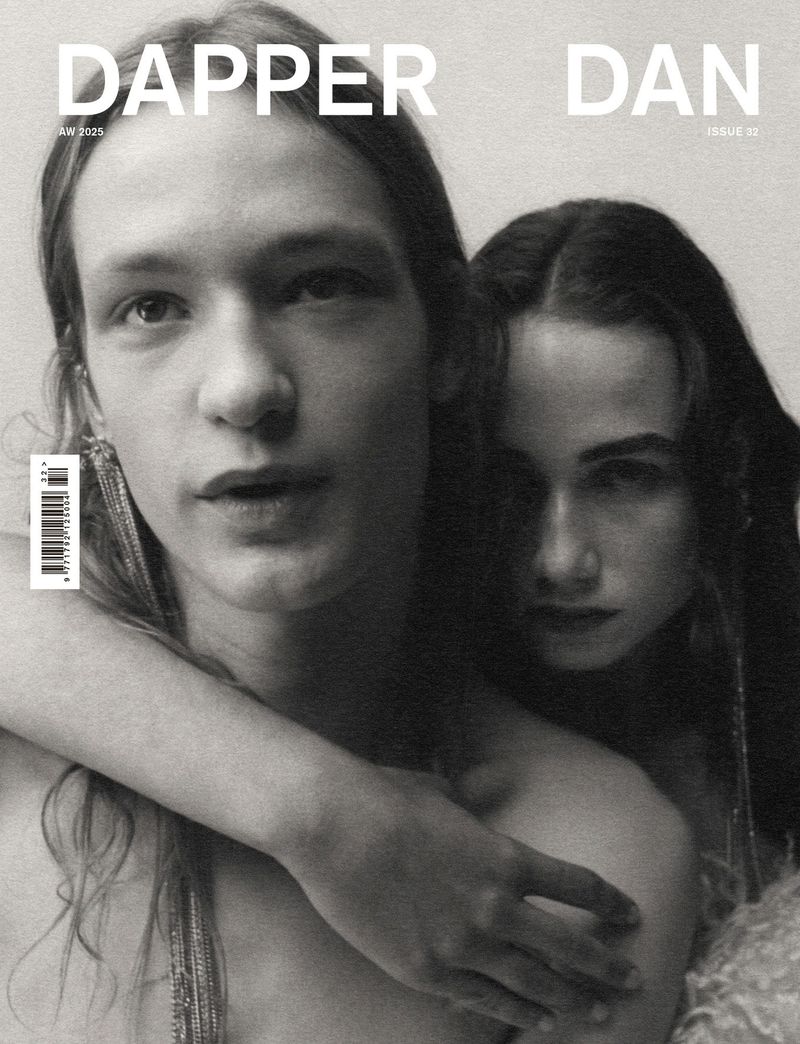 Black and white portrait of two models with long hair embracing against a neutral backdrop on a magazine cover.