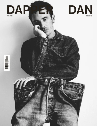 Black and white magazine cover featuring a seated man wearing a denim jacket and holding out the waistband of oversized denim jeans.