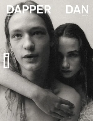 Black and white portrait of two models with long hair embracing against a neutral backdrop on a magazine cover.