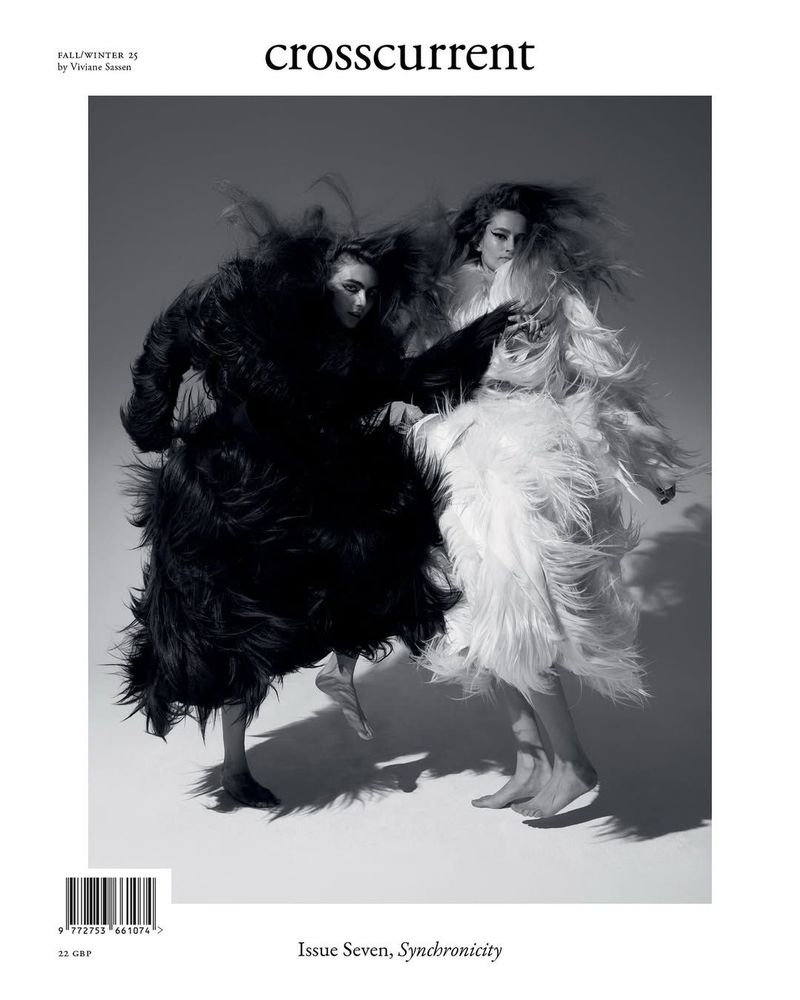 Editorial fashion shot featuring two women in contrasting black and white feathered coats, full-length on a light grey background. 