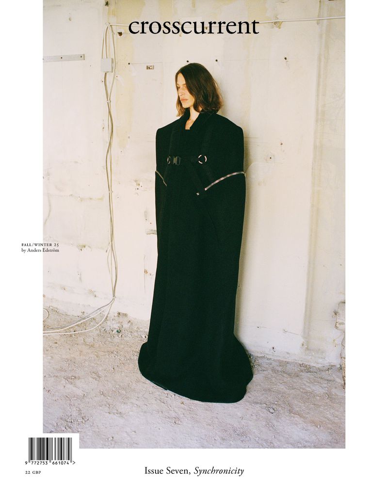 Magazine cover featuring a model in a black, avant-garde coat against a textured wall with visible wiring and minimalist aesthetic.