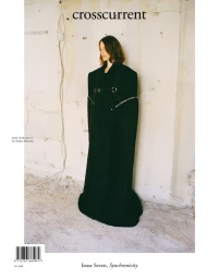 Model wearing an oversized floor-length black structured coat against a raw unfinished wall on the Crosscurrent Issue Seven cover.