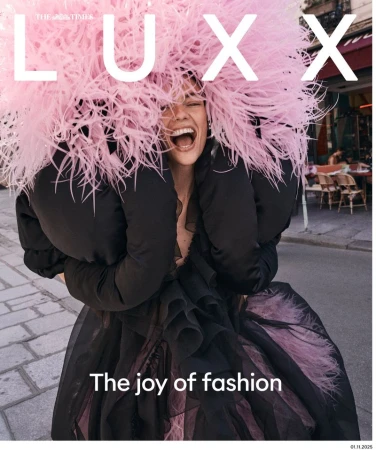 Model Beauïse Genç laughing in a voluminous pink feather headpiece and black ruffled dress on a paved city street.