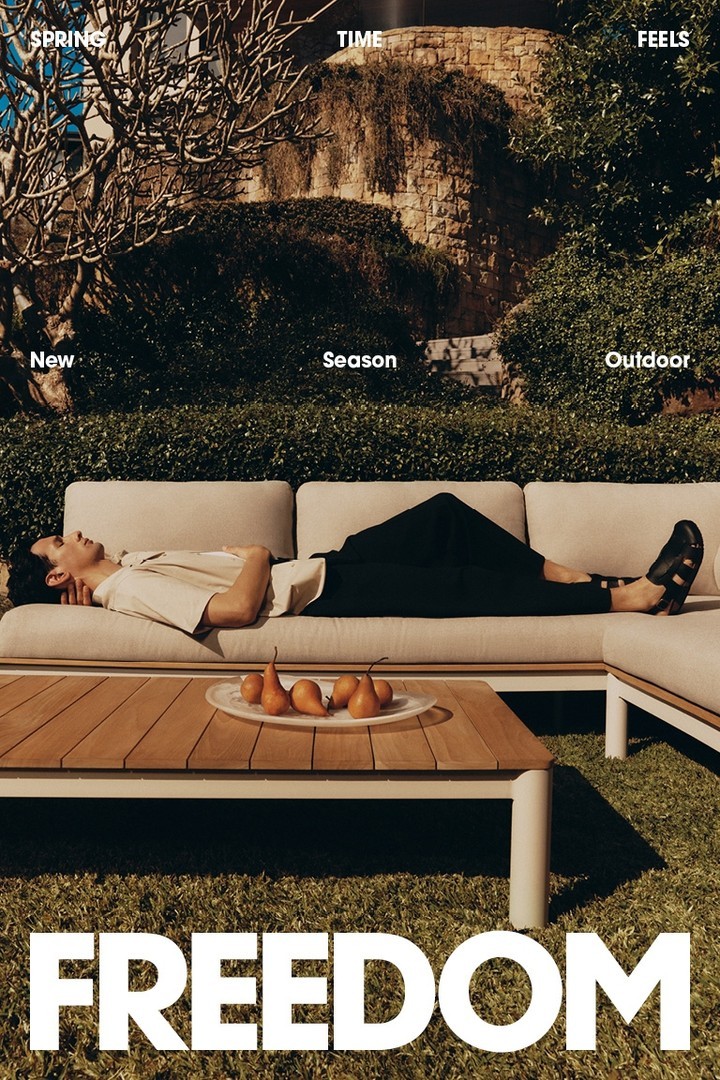 Man lounges on outdoor sofa next to pears and wooden table in garden setting with green grass and plants in natural sunlight.