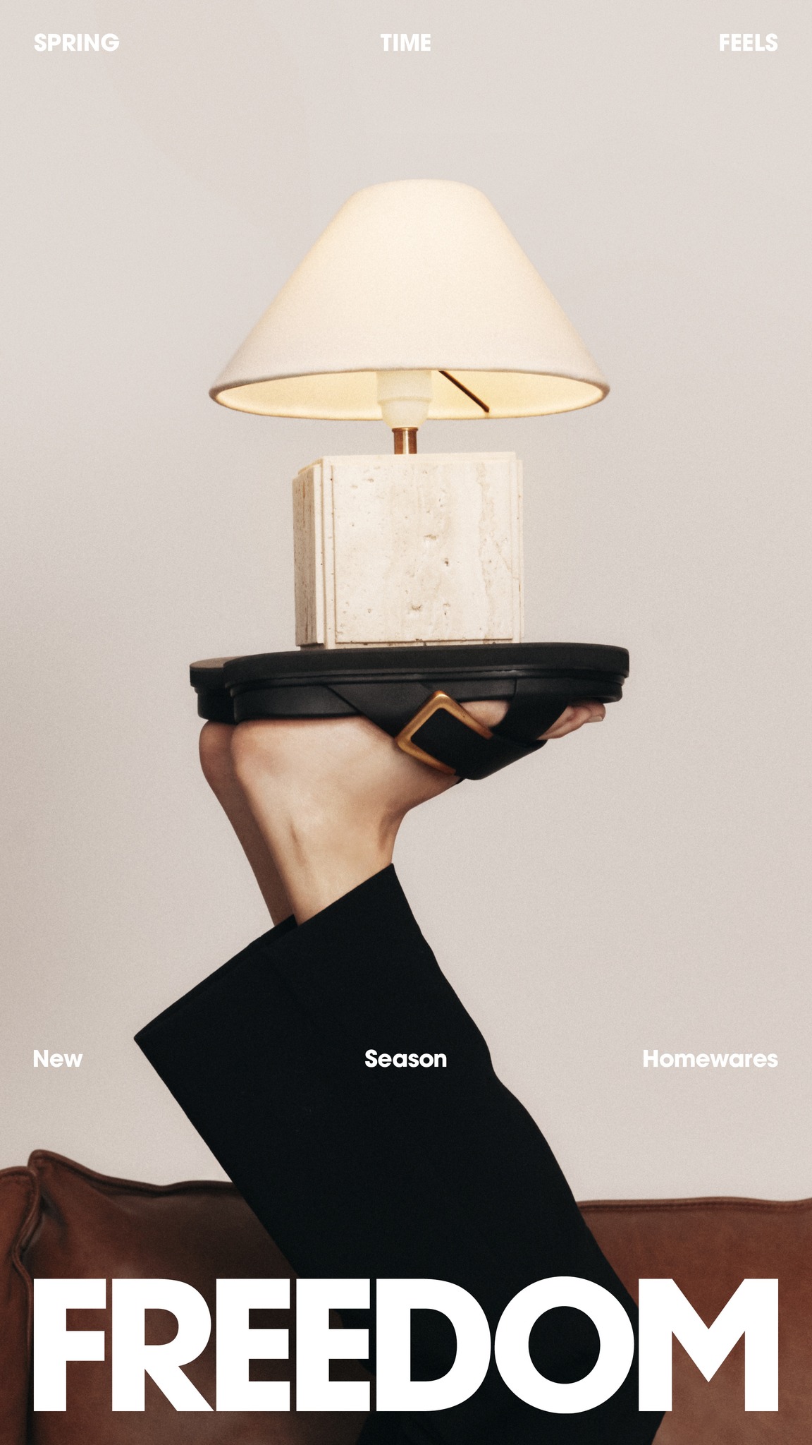 Conceptual fashion shot of a lamp sitting atop a sandal held by a person against an off-white background. Freedom text at bottom.
