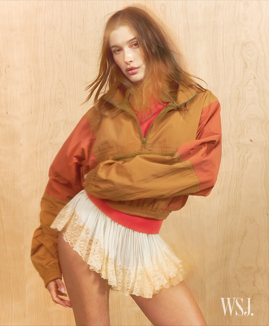 Hailey Bieber wearing a brown windbreaker and white lace skirt against a wooden wall for WSJ November 2025 Covers.