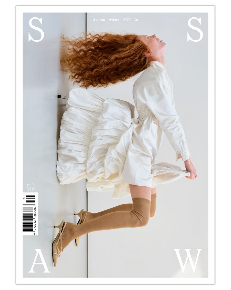 Fashion magazine cover featuring a woman in a white dress and heels, with a red hair. Shot in a photo studio with soft lighting.