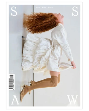 Redhead model in a voluminous white tiered dress and beige slingback heels suspended mid-air against a bright white background.