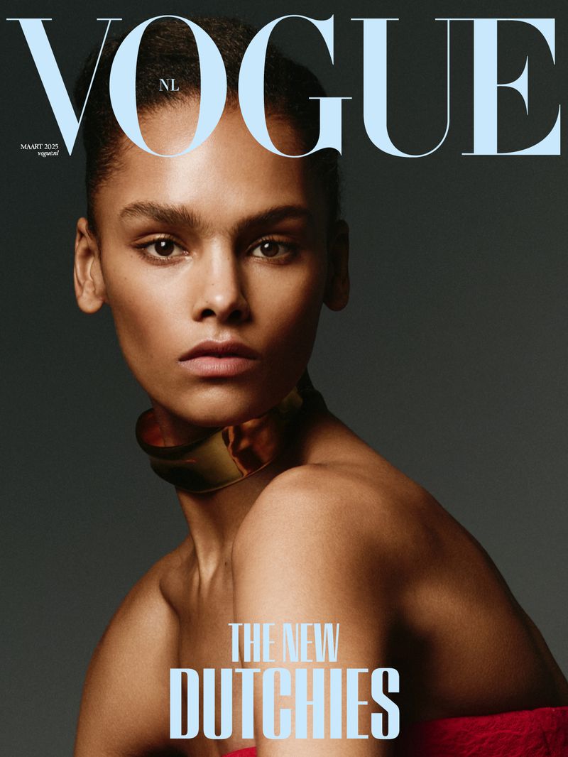Vogue NL cover featuring a portrait of an adult female model with dark hair and a gold collar necklace against a gray background.
