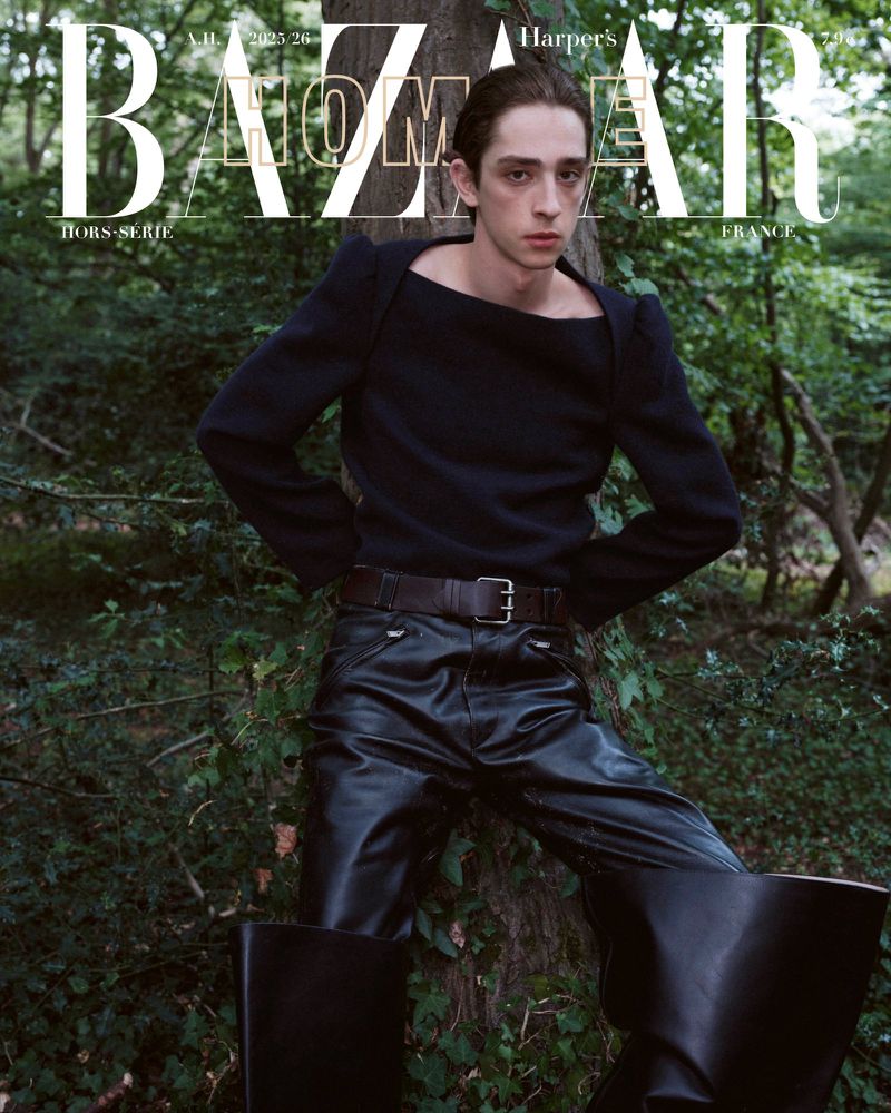 Magazine cover featuring a model in black sweater and leather pants, posing near a tree in a wooded area with the 'BAZAAR' logo.